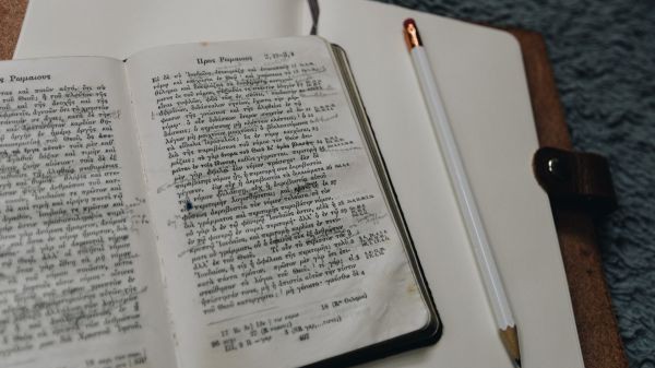 Aufgeschlagene Bibel in griechischer Sprache mit Notizbuch und Stift.