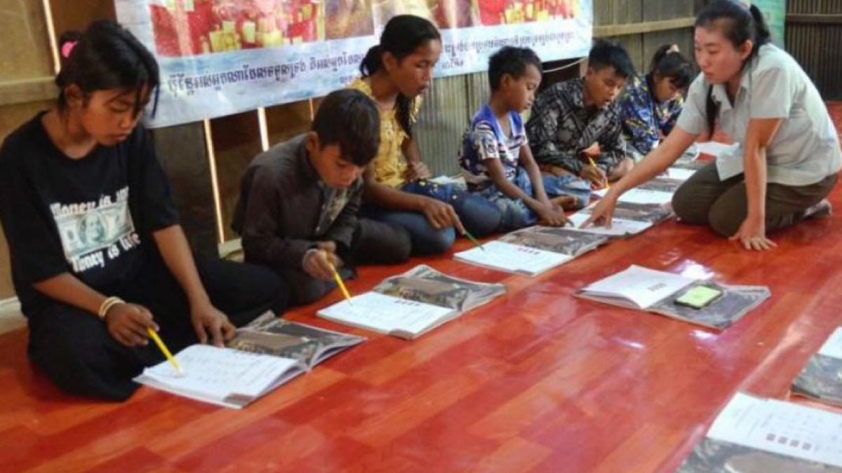 Junge Menschen sitzen vor einem geöffnetem Buch am Boden und lesen laut vor.