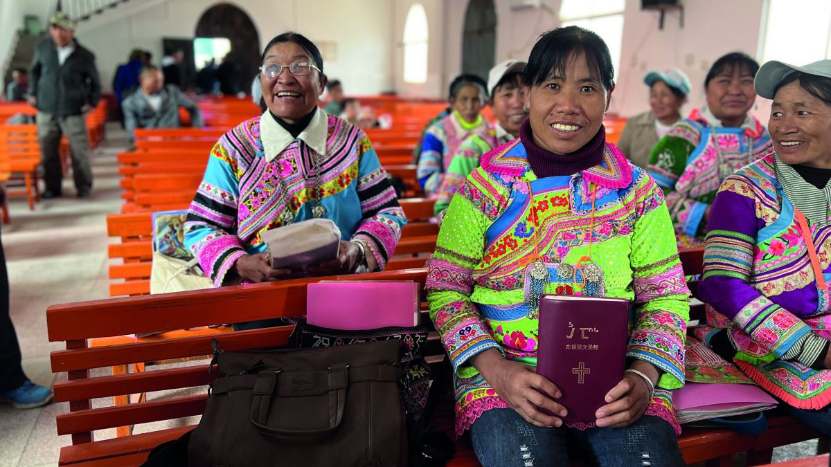 In einer Kirche sitzen Chinesische Frauen in bunter Kleidung und zeigen Bibeln in die Kamera