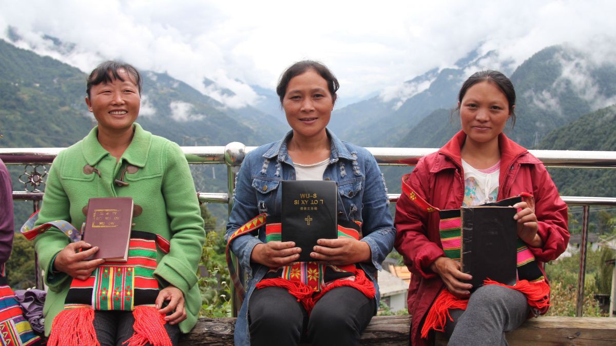 Drei chinesische Damen sitzen mit einer Bibel in den Händen vor einem Gebirgszug.