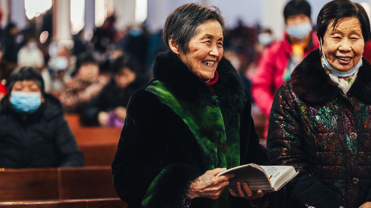 Zwei chinesische Damen. Eine hält eine Bibel in der Hand und lächelt.