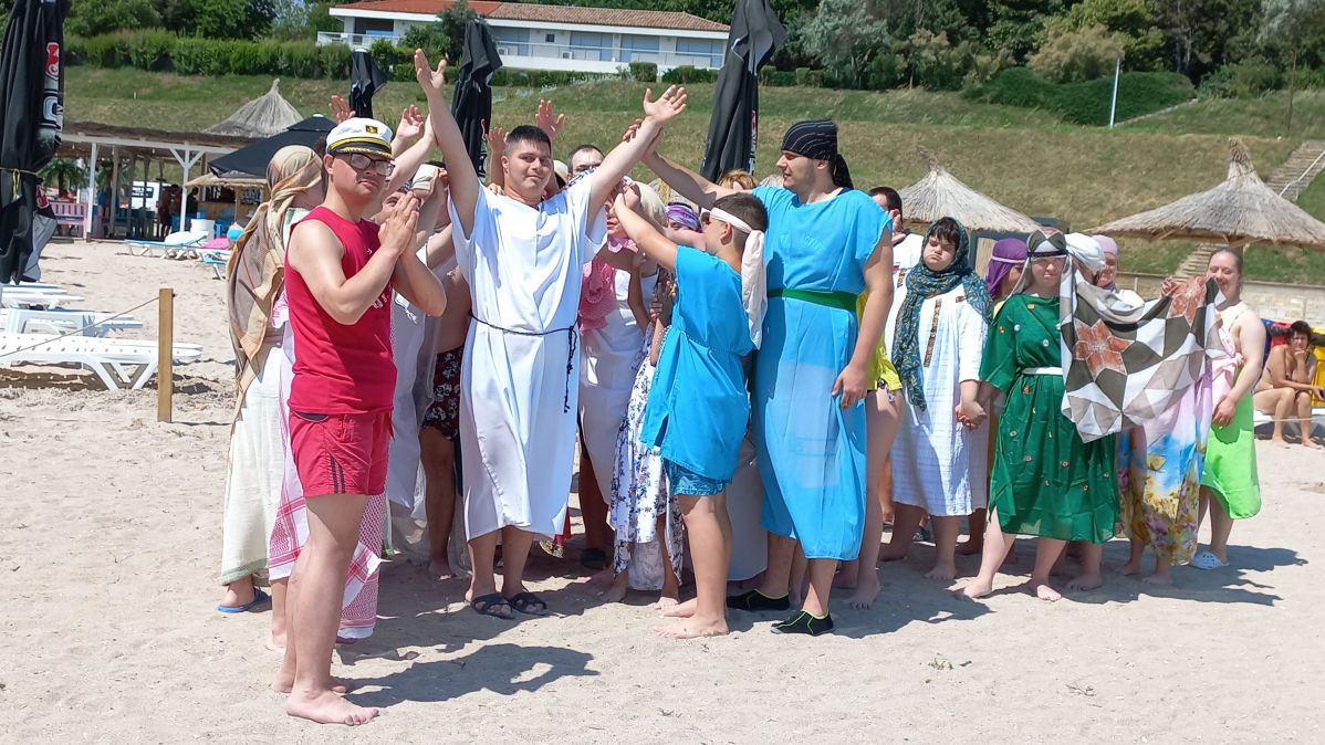 Eine gruppe junger Menschen mit Down-Syndrom stehen verkleidet am Strand und stellen die biblische Szene der Sturmstillung nach.