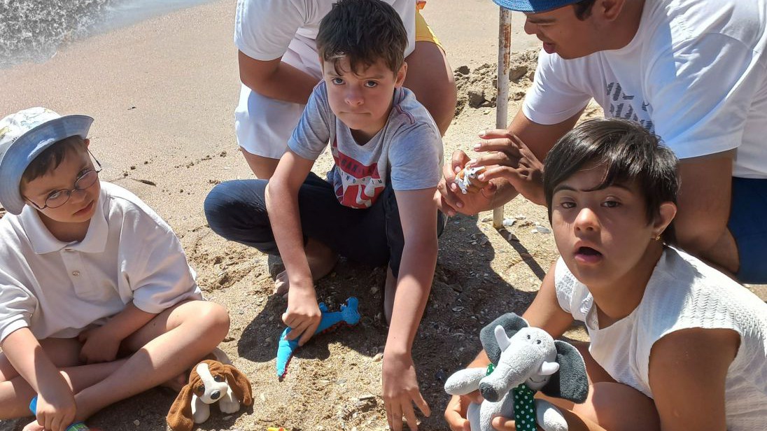 Kinder mit Down-Syndrom verkleidet am Strand. Sie spielen mit Plüschtieren die Geschichte von Noah und der Flut nach