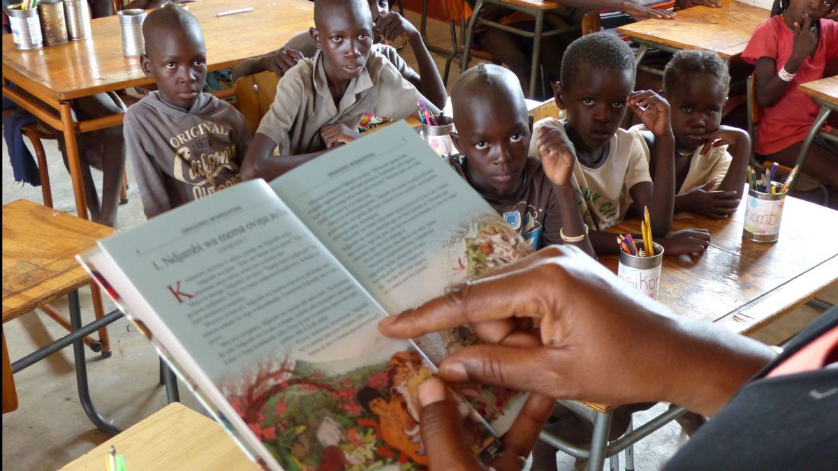 Im Vordergrund ist eine aufgeschlagene Kinderbibel zu sehen aus der gerade vorgelesen wird. Im Hintergrund sitzen fünf junge Menschen und lauschen gespannt den biblischen Geschihten.