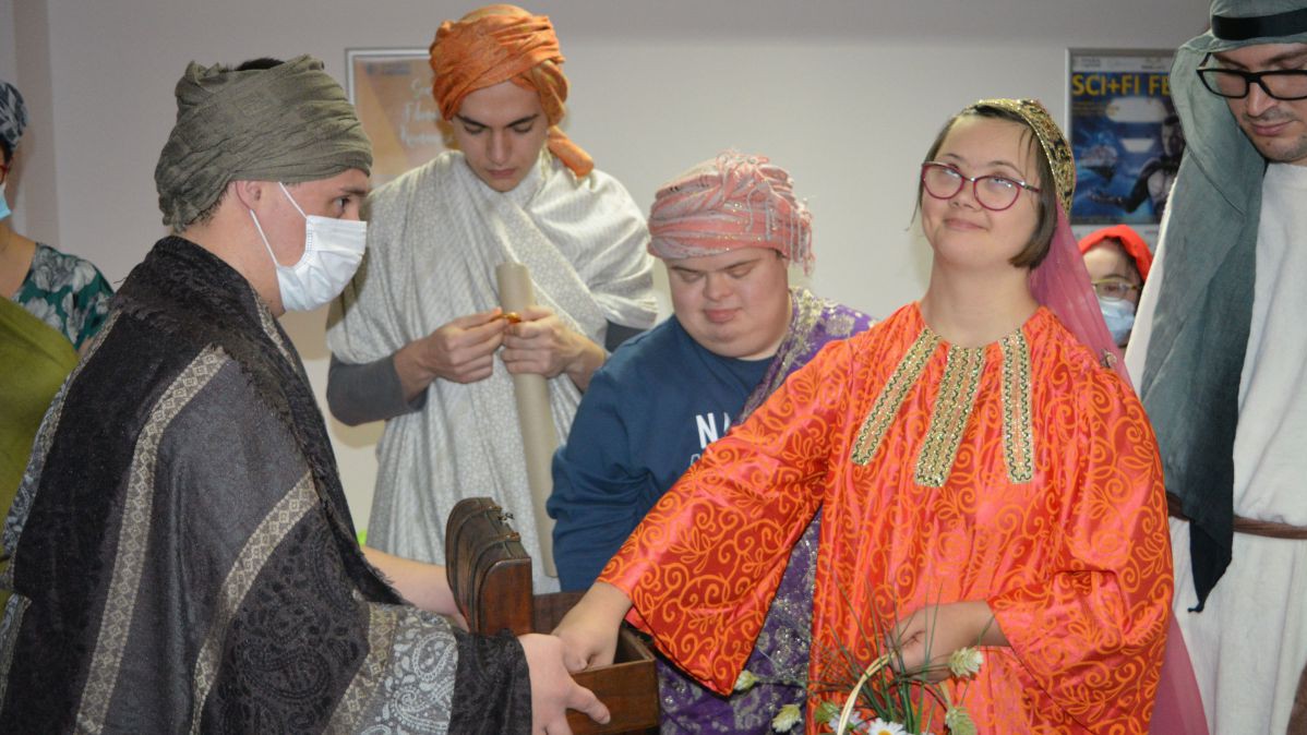 Menschen verkleidet als biblische Figuren. Ein Mädchen in einem orangenem Kostüm greift in eine geöffnete Schatzkiste, die eine andere Person in Händen hält.