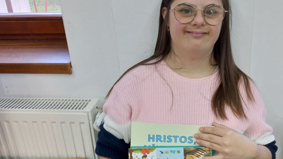 Eine junge Frau mit Down-Syndrom hält hält stolz ein Malbuch mit Geschichten aus dem Leben Jesu in der Hand.