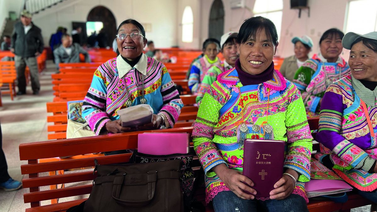 In einer Kirche sitzen Chinesische Frauen in bunter Kleidung und zeigen Bibeln in die Kamera