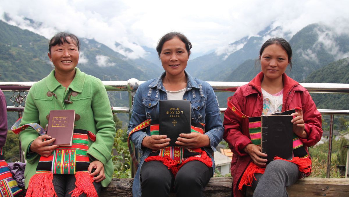 Drei chinesische Damen sitzen mit einer Bibel in den Händen vor einem Gebirgszug.