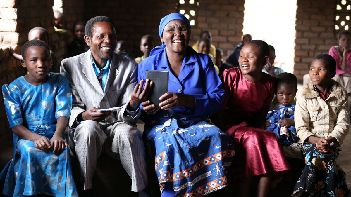 Eine Familie, die Elhomwe spricht, sitzt in farbenfrohen Kleidern in der Kirche und hält stolz das Neue Testament in Händen.