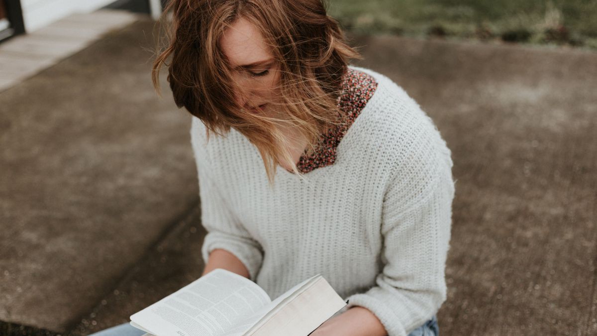 Junge Frau mit weißem Pullover liest eine Bibel.