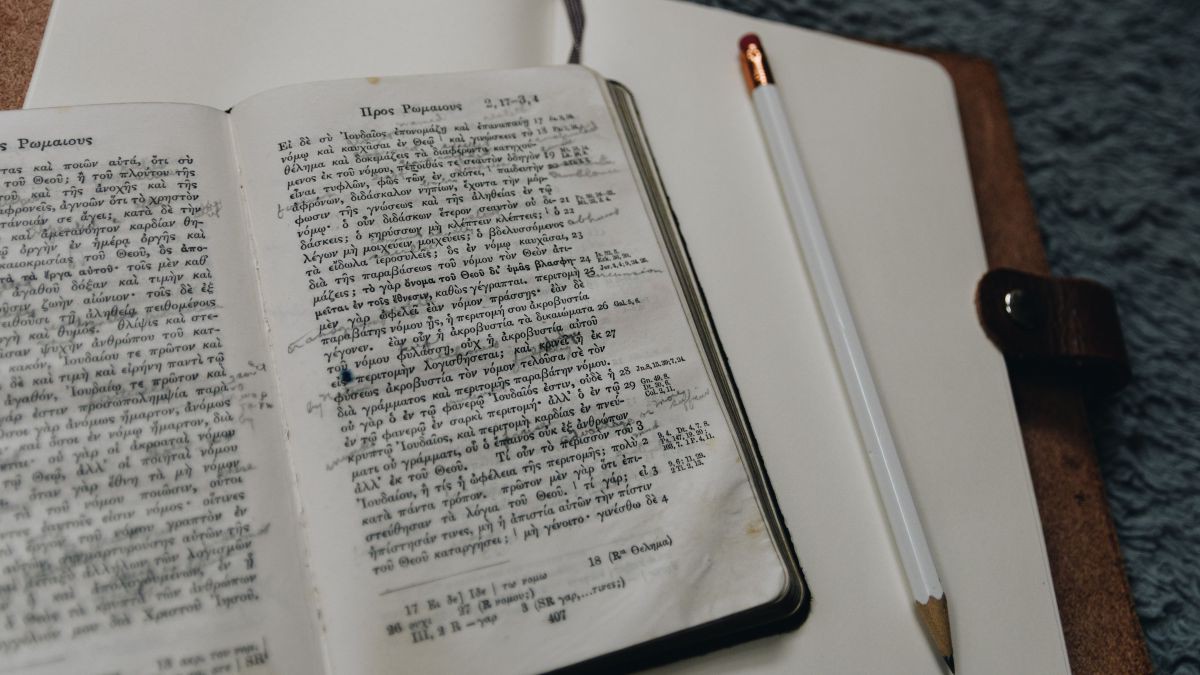 Aufgeschlagene Bibel in griechischer Sprache mit Notizbuch und Stift.