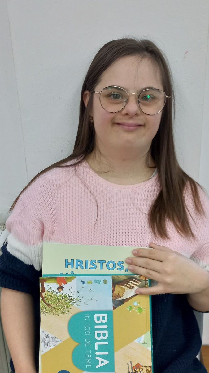 Eine junge Frau mit Down-Syndrom hält hält stolz ein Malbuch mit Geschichten aus dem Leben Jesu in der Hand.