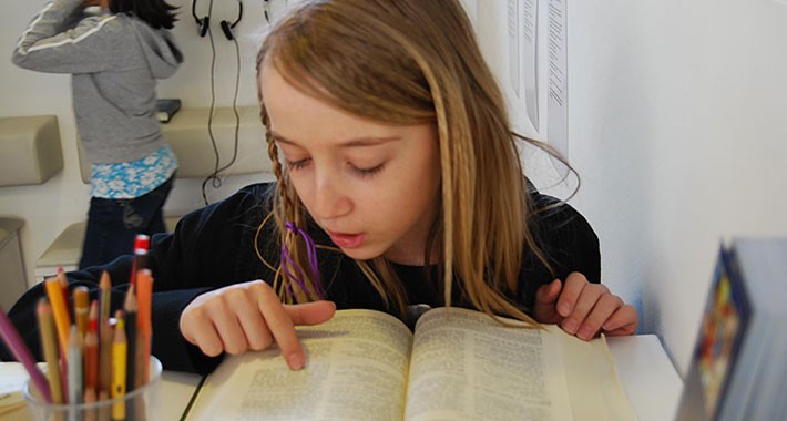Mädchen liest in einer Bibel und zeigt mit ihrem Zeigefinder auf eine Bibelstelle