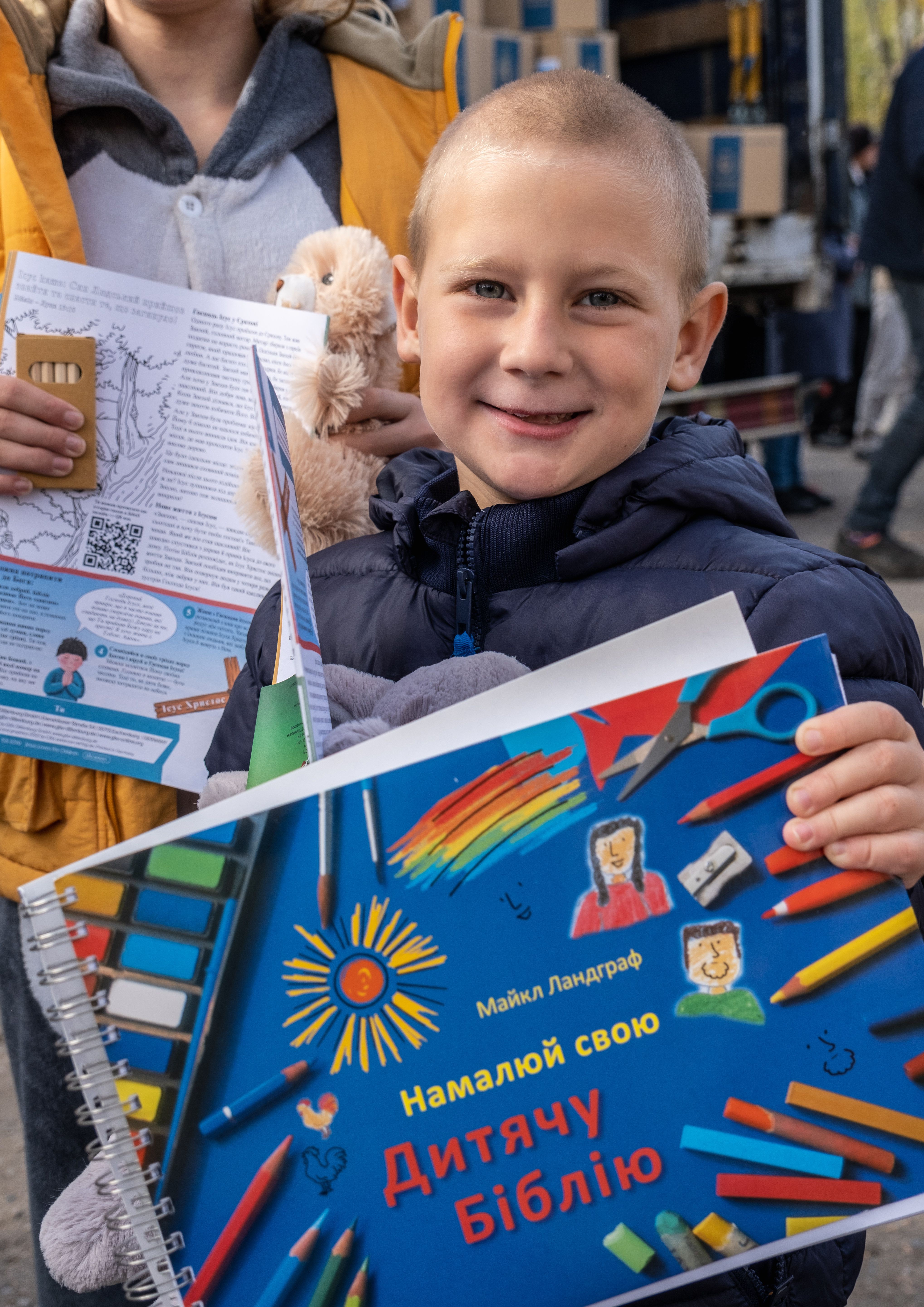 Ein Junge in Winterjacke hält eine Kinderbibel zum Selbstgestalten in die Höhe