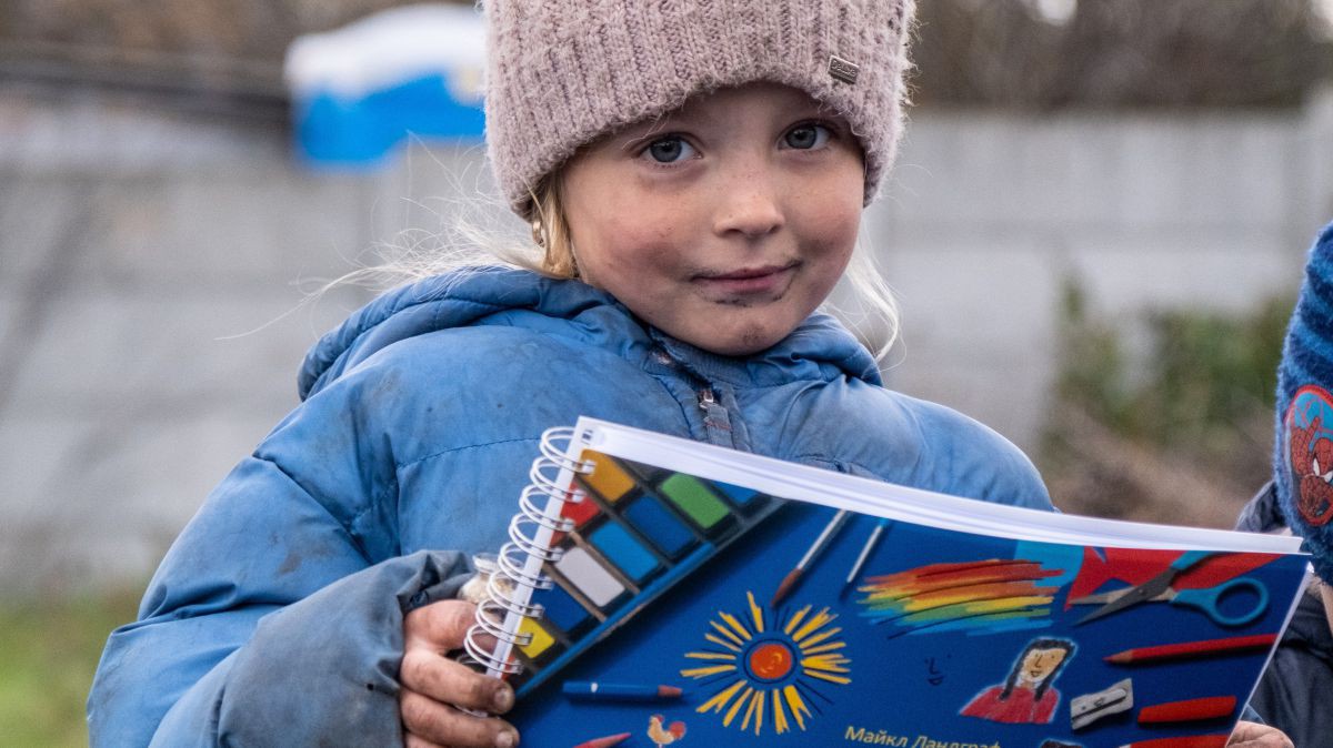 Ein Mädchen in dicker Winterjacke und Wollmütze hält eine Kinderbibel zum Selbstgestalten in der Hand