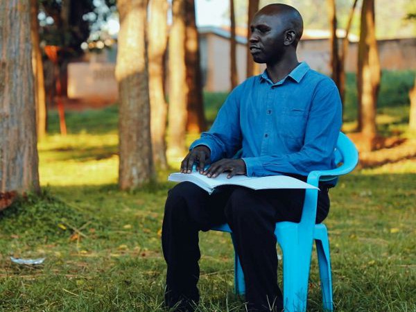 Patrick Owiyo liest in einem Band der Braille-Bibel in Acholi