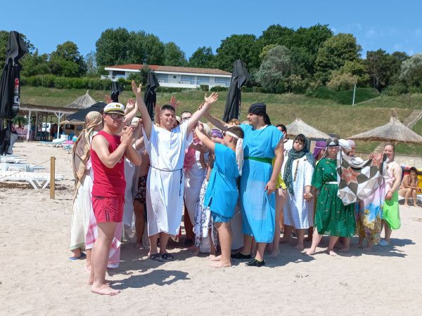 Eine gruppe junger Menschen mit Down-Syndrom stehen verkleidet am Strand und stellen die biblische Szene der Sturmstillung nach.